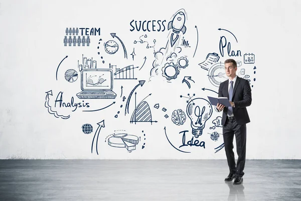 Office man in suit with notebook in hands, standing near business strategy plan on white wall, concrete floor. Doodle drawing with arrows, graphs and network icons. Concept of business idea