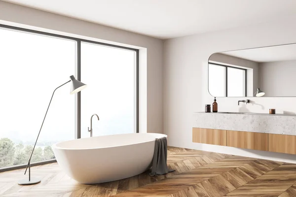 White and wooden bathroom interior with white tub with lamp, sink with mirror, parquet floor. Modern interior and window with countryside, 3D rendering no people