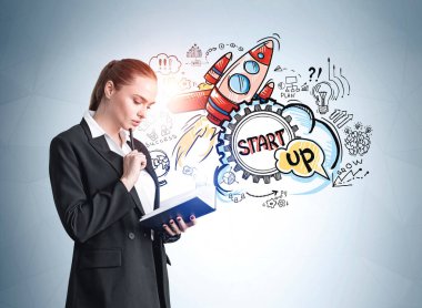 Ofisteki kadın defter okuyor, dalgın dalgın bakıyor. Roket başlatma simgeleri mavi duvarda, yeni bir ürünün tanıtımı. Yeni proje ve iş fikri kavramı