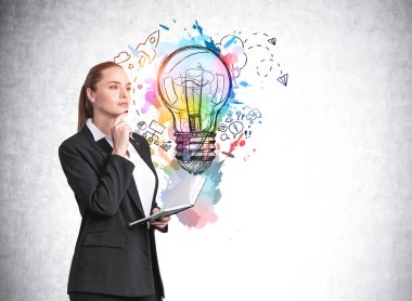 Resmi olarak Avrupalı çekici genç bir kadın elinde not defteri tutarak üzerinde renkli iş lambası çizimi olan beton duvarın yanında kafa yoruyor. Yaratıcılık ve beyin fırtınası kavramı