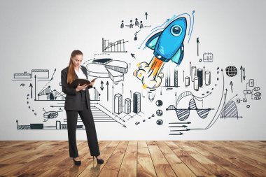 Ellerinde parke zemininde not defteri olan bir ofis kadını. Gri duvardaki iş stratejisi planı, grafik değişiklikleri ve roketle çizim. Başlangıç ve finans kavramı