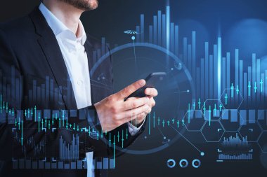 Ofis çalışanı, elinde telefon, cep telefonu kullanıyor. Şamdanlar ve bar tablosu olan borsa simgeleri. Teknoloji ve çevrimiçi ticaret kavramı