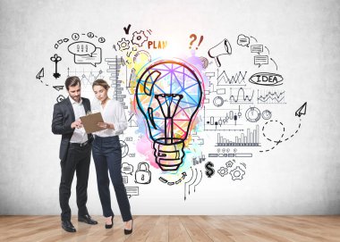 İş adamı ve iş kadını resmi giysiler içinde ellerinde pano ve renkli iş fikri ampulü taslağıyla yakınlardaki beton duvara beyin fırtınası yapıyorlar. Yaratıcılık kavramı ve başlangıç. Tam uzunluk