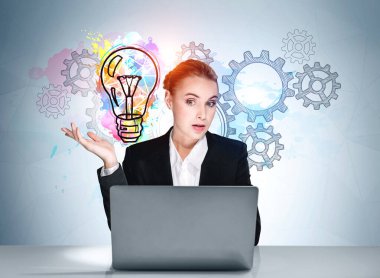 Portrait of amazed attractive business woman in formal wear sitting at the desk in front of laptop, light blue wall with colorful light bulb and cog wheels sketch. Launch a new business start up