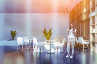 Evdeki çekici genç bayanın ön görüntüsü broşür telefon takıyor, otel kantininde ve iş yerinde duruyor. Modern ortak alan, misafir tesisleri. Güneş ışınları ve mercekler odayı dolduruyor.