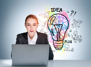 Resmi olarak giyinmiş çekici bir iş kadını portresi dizüstü bilgisayarın önünde oturuyor, açık mavi duvarda renkli ampul çizimi var. Yeni bir iş kurma fikri başlat