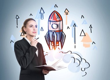 Not defteri ve kalemle girişimi merak eden düşünceli çekici iş kadınının portresi. Başarı kavramı ve yeni iş projeleri. Renkli roket çizimi