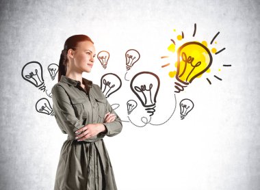 Kollarını kavuşturmuş gündelik giysiler içinde gülümseyen Avrupalı çekici genç kadın, yeni iş fikirleri ve başlangıç hakkında kafa yoruyor. Beton duvardaki ampullerin çizimi.