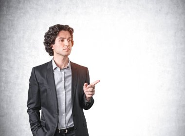 Takım elbiseli kendine güvenen İspanyol işadamı parmağını gösterip şirketin satışlarındaki büyümeyi düşünüyor. Beton duvar arkaplanı