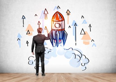 Rear view of businessman in suit drawing start up sketch on concrete wall. Launch a new business. Concept of success. Colorful rocket sketch