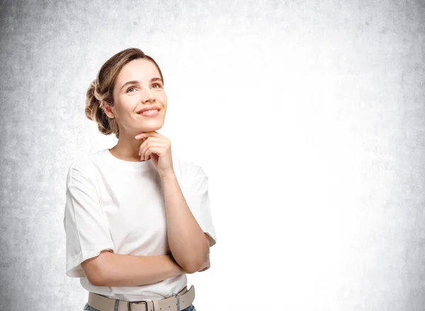 キャリアの機会と新しいビジネスアイデアについて考えるカジュアルな白いTシャツの笑顔ヨーロッパの魅力的な若い女性の肖像画 背景のコンクリート壁 — ストック写真