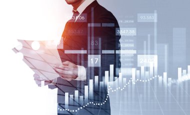 Resmi takım elbise giyen genç işadamı ayakta duruyor ve gazete okuyor. Finansal tablolar, bar şemaları ve ön plandaki grafikler. Başarılı ticaret için yeni strateji arama kavramı
