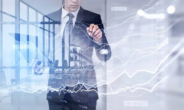 クリップボードを保持する正式なスーツを身に着けているビジネスマンはペンで財務グラフに触れている 株式市場の行動を分析する概念 背景にパノラマ窓のあるオフィス — ストック写真