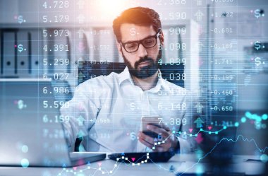 Beyaz gömlekli iş adamı hesap makinesine güveniyor ve elinde akıllı telefon tutuyor. Bilgisayarı ve masası arka planda olan ofis işyeri. Finansal tablo ve grafik arka planda. Ticaret kavramı