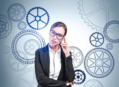 Resmi takım elbise giyen düşünceli iş kadını şirket için yeni yaratıcı fikirler düşünüyor. Arka planda dişli çarklı duvar. Modern teknoloji ve ilham kavramı