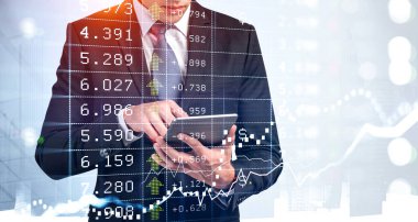 Resmi takım elbiseli bir işadamı tablete yazı yazıyor. Arka planda şehir merkezindeki gökdelenler. Finansal tablo ve grafik ön planda. Başarılı ticaret stratejisi kavramı