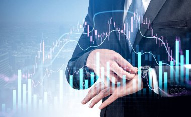 Resmi takım elbiseli bir işadamı saati kontrol etmek için saatlere dokunuyor. Arka planda New York gökdelenleri var. Ön planda eski şamdan ve finansal grafik var. Ticaret kavramı
