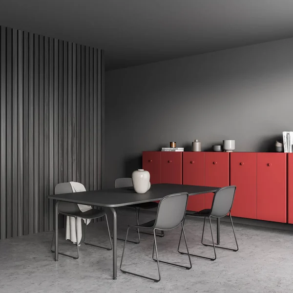 Corner of the black dining table in the grey living room interior with the accent red sideboard. Dark wood wall panelling, concrete flooring. Minimalist design. 3d rendering