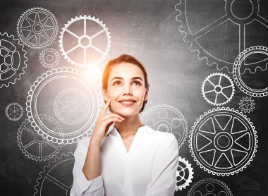 Beyaz gömlek giyen gülümseyen iş kadını şirket için yeni yaratıcı fikirler düşünüyor. Arka planda çarkıfelek olan tebeşir tahtası. Modern teknoloji ve ilham kavramı