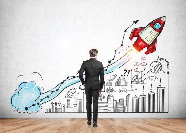 Resmi takım elbiseli iş adamı, beton duvarında büyük bir roket fırlatma, iş, plan, takım çalışması, bar ve pasta diyagramı olan renkli çizimin yanında duruyor. Yaratıcı fikirler için hayal gücü kavramı