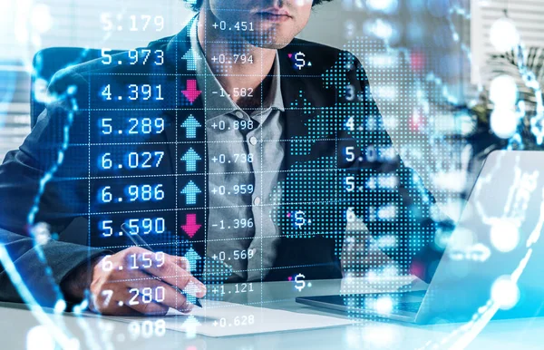 正式なスーツを着たビジネスマンが紙にメモを取っている 背景にノートパソコン付きのオフィスワークスペース 金融チャートと仮想世界の前景 国際的な成功取引の概念 — ストック写真
