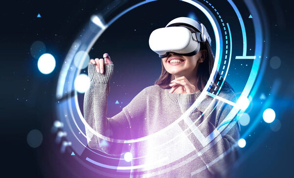 Smiling businesswoman in green sweater wearing vr helmet. Digital interface with circle hologram. Dark blue background. Concept of future technology and entertainment playing game in virtual reality