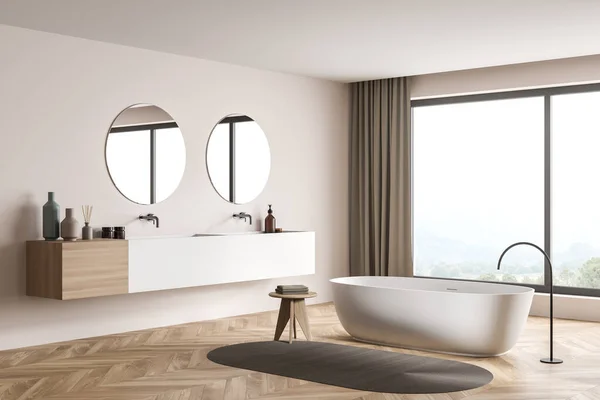 Corner view of a beige bathroom interior with a panoramic view, trendy details, a white ceramic bath, a rug, a modern vanity, two round mirrors and parquet flooring. Minimalist design. 3d rendering