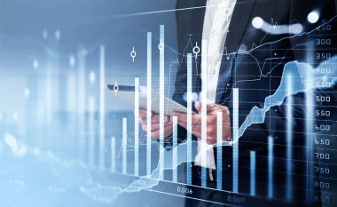 Resmi takım elbiseli bir işadamı elinde tablet tutuyor. Arka planda bulanık ofis işyeri var. Finansal grafik, grafik ve çizelge ön planda. Başarılı ticaret kavramı