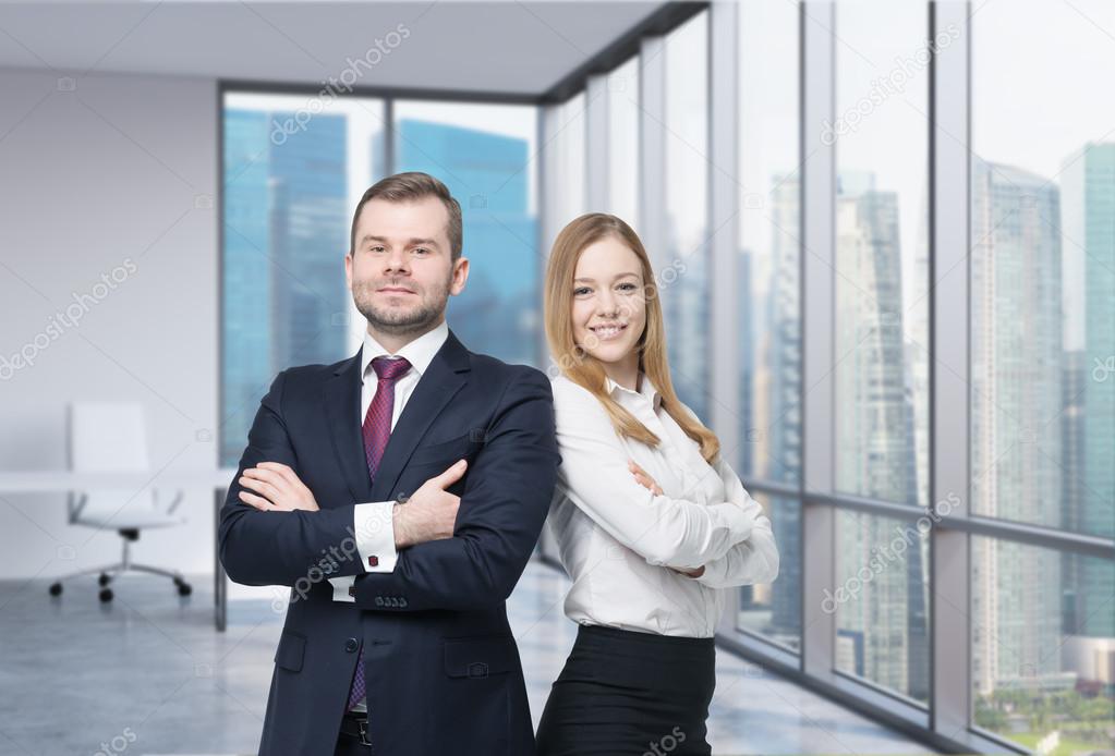 Happy young couple of professionals are standing in a contemporary glass office in New York.