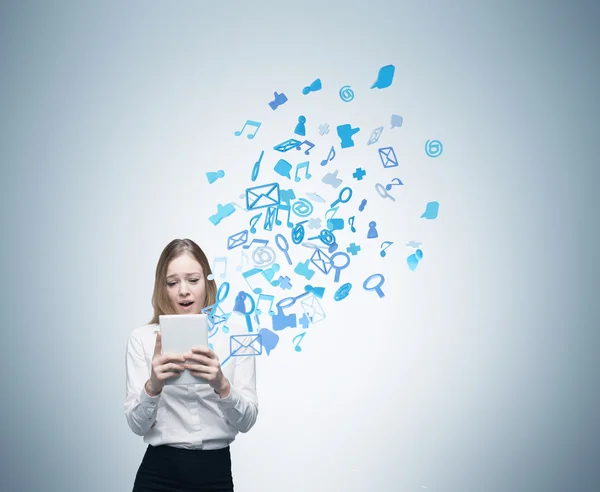 Beautiful young business woman is looking at the tablet. Flying out social media icons. — Stock Photo, Image