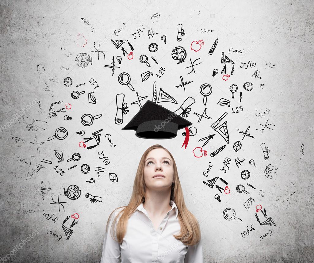 Young beautiful business woman is thinking about education at business school. Drawn business icons over the concrete wall. Graduation hat.