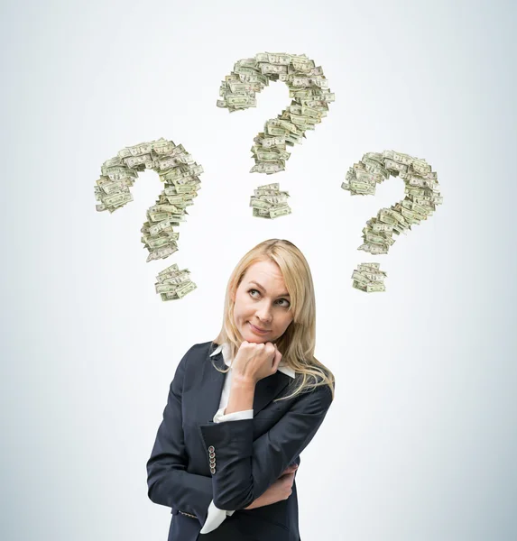 Beautiful blonde business woman is thinking about business ideas. Three question signs are made of dollar notes. — Stock Photo, Image