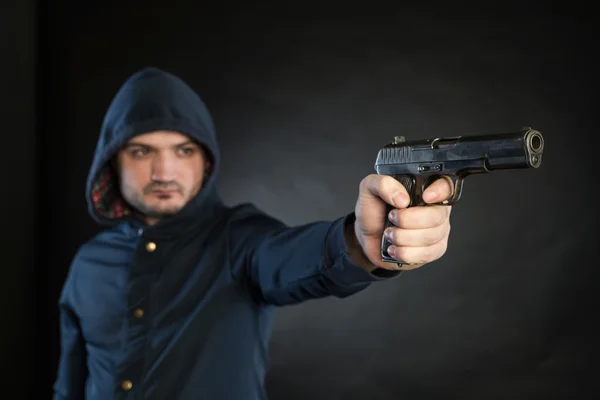 Un hombre armado con una sudadera con capucha apunta con una pistola al objetivo. . —  Fotos de Stock