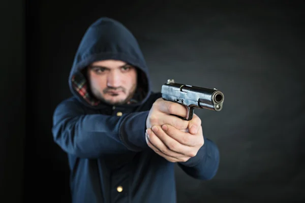 Bewaffneter Mann im Kapuzenpullover richtet Handfeuerwaffe auf Zielscheibe. — Stockfoto