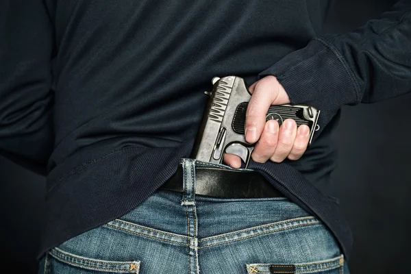 Eine Person versteckt eine Handfeuerwaffe unter dem Jeansgürtel. — Stockfoto