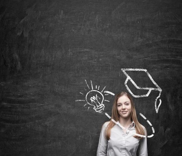 Young beautiful business woman is thinking about education at business school. Drawn graduation hat and light bulb over the concrete wall. A concept of the usefulness of business education. — Stock fotografie
