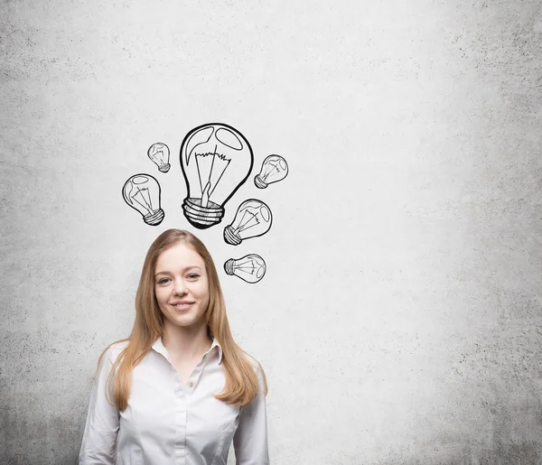 Smiling young beautiful business lady is thinking about new innovative ideas. Light bulbs are drawn on the concrete wall behind the lady.