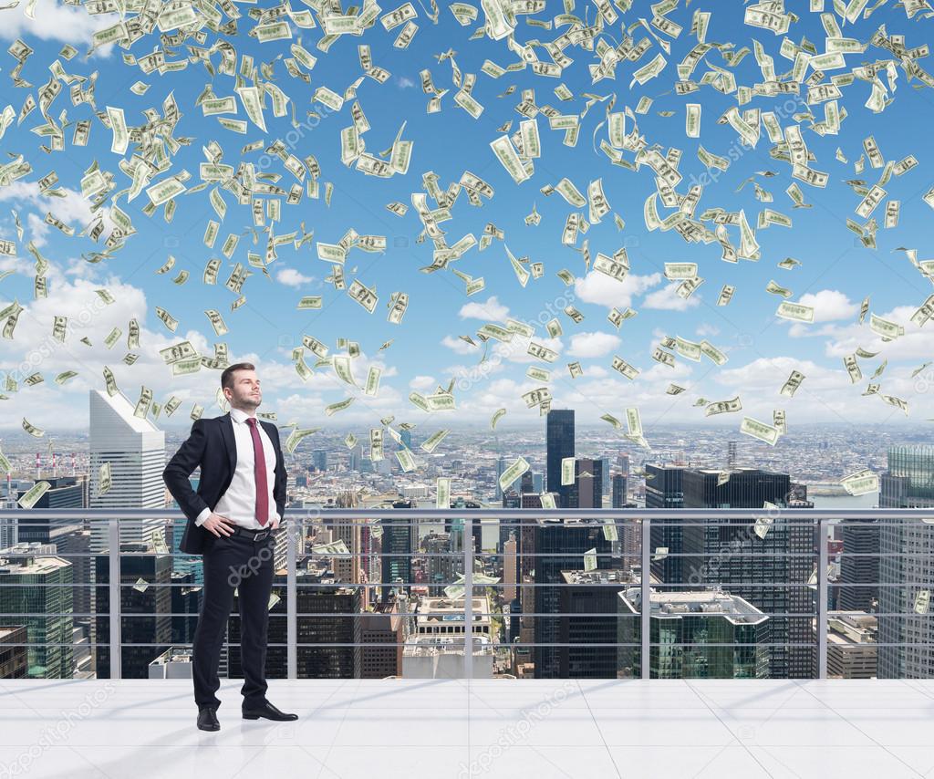 Confident handsome businessman is standing on the roof terrace in New York City. Falling dollar notes from the sky. A concept of financial consultancy.