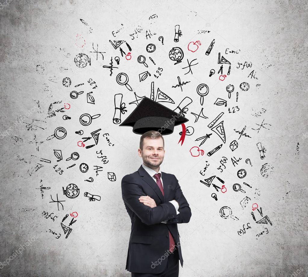 Young handsome businessman is thinking about education at business school. Drawn business icons over the concrete wall. Graduation hat.