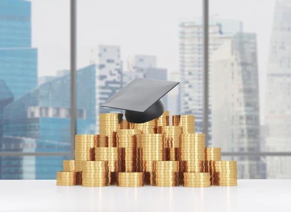 Graduation hat is laying on the coins pyramid. A concept of a high price for the university education. Panoramic lecture theatre background. — Stock Photo, Image