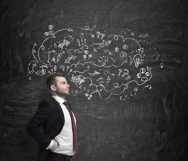 Hombre de negocios guapo y seguro está mirando a través de los problemas del proceso de desarrollo de negocios. Iconos de negocios se dibujan en la pared oscura . — Foto de Stock