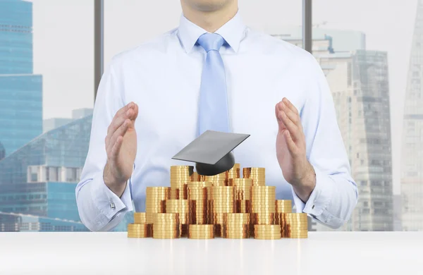 Studenten är att placera händerna över avläggande av examen hatt och mynt pyramiden. Ett koncept för ett högt pris för universitetsutbildningen. New York bakgrund. — Stockfoto