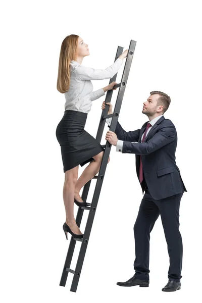 Молодой привлекательный бизнесмен держит лестницу для леди в формальной одежде, чтобы подстегнуть ее идеи. Концепция успеха и командной работы — стоковое фото
