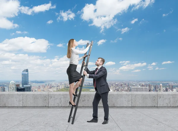 El hombre de negocios tiene una escalera para la dama de negocios. El concepto del trabajo en equipo. En la terraza de la azotea en Manhattan, Nueva York. Cayendo dólares del cielo . —  Fotos de Stock