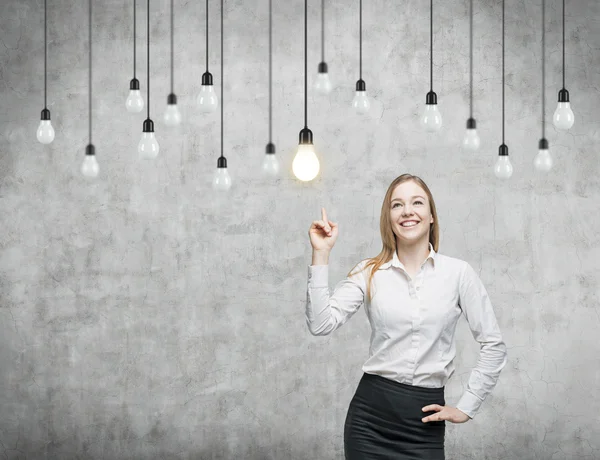 Business woman is pointing out the light bulbs. The concept of the innovative business strategy. Concrete background. — Stock Photo, Image