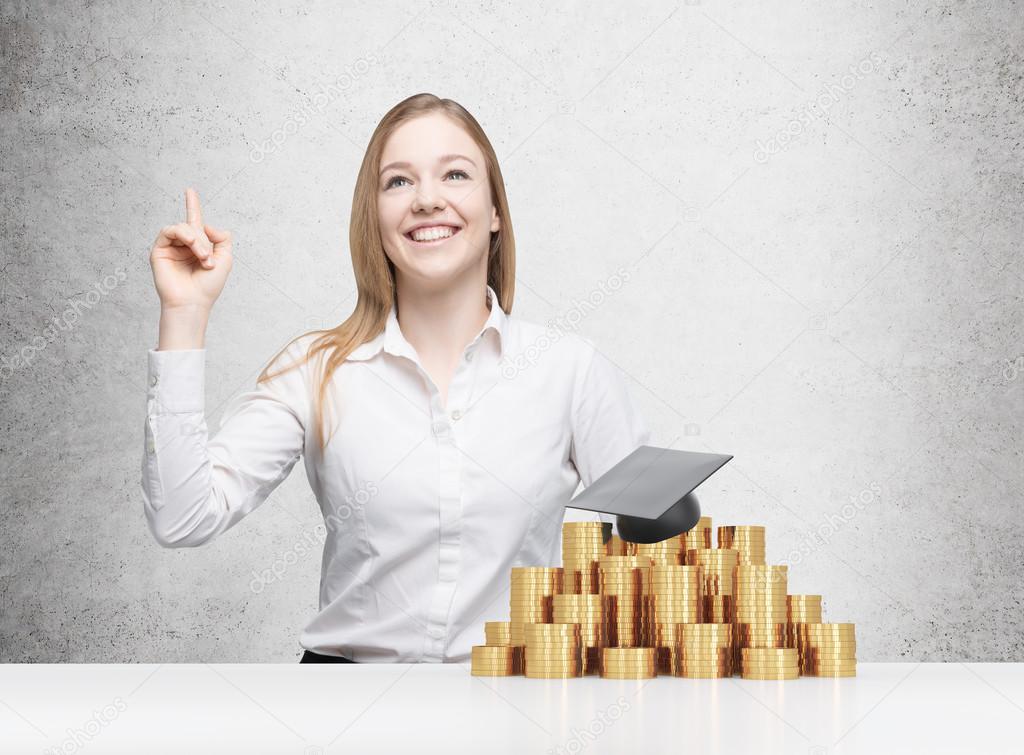 Beautiful blonde girl is thinking about university education. Graduation hat is laying on the coins pyramid.