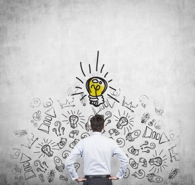 Dikiz yeni fikir bulmaya çalışan genç Yöneticisi. İş ikonları/simgeleri ve sarı bir ampul beton duvara çizilir.