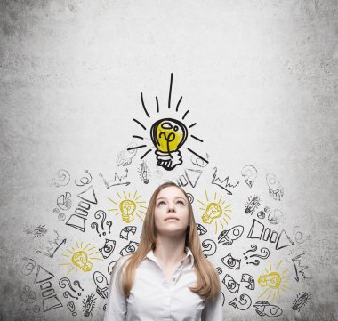 Young beautiful lady is looking at the drawn yellow light bulb. The concept of the brainstorm of start up business.Concrete wall. clipart