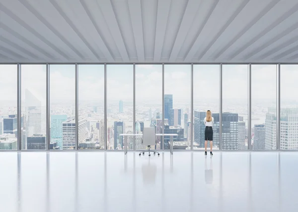 Rear view of the blonde employee who looks out the window in New York's panoramic office. A concept of the modern workplace. — Stock Photo, Image