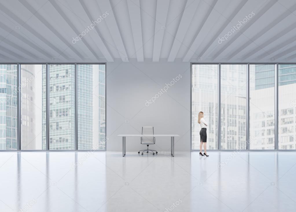 Side view of the blonde employee who looks out the window in New York's panoramic office. A concept of the modern workplace.